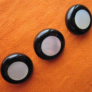 Könnte beinhalten: Drei schwarze Knöpfe mit weißen Mittelpunkten. Die Knöpfe haben eine glatte, glänzende Oberfläche.