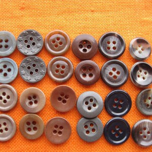 Könnte beinhalten: Sortiment von 20 braunen, grauen und schwarzen Knöpfen mit vier Löchern. Die Knöpfe sind in Reihen auf einem orangefarbenen Stoffhintergrund angeordnet.