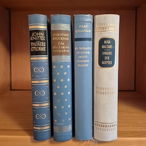 Könnte beinhalten: Vier Hardcover-Bücher stehen aufrecht nebeneinander. Das erste ist blau mit goldenen Unendlichkeitssymbolen und dem Text John Knittel Therese Etienne. Das zweite ist blau mit goldenen Blumen und dem Text Christine Brückner Ebe die Spuren verweben. Das dritte ist blau mit dem Text Olav Gullvaag Es begann in einer Mittsommernacht. Das vierte ist hellgrau mit dem goldenen Text Mika Waltari Sinuhe der Ägypter.