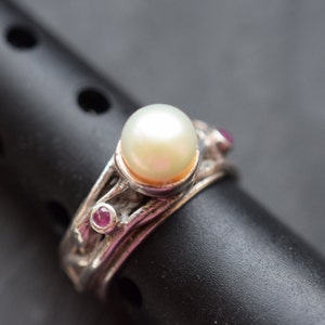 Könnte beinhalten: Ein silberner Ring mit einem großen weißen Perlmutt und zwei kleinen rosafarbenen Edelsteinen.