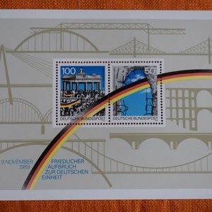 Könnte beinhalten: Ein vintage deutsches Briefmarkenset zur Erinnerung an die friedliche Wiedervereinigung Deutschlands am 9. November 1989. Die Briefmarken zeigen Bilder des Brandenburger Tors und eines Abschnitts der Berliner Mauer. Die Briefmarken sind von einem Brückenmotiv umgeben, das die Verbindung zwischen Ost- und Westdeutschland symbolisiert.