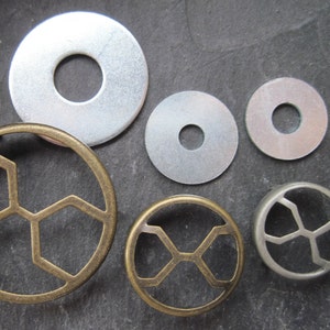 Könnte beinhalten: Sortiment aus Metall-Unterlegscheiben und dekorativen Metallringen. Die Unterlegscheiben sind silberfarben und haben ein Loch in der Mitte. Die Ringe sind golden und haben ein sechseckiges Muster.