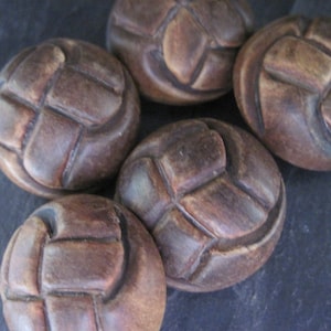 Könnte beinhalten: Fünf braune Keramikknöpfe mit einem gewebten Design. Die Knöpfe sind rund und haben eine erhabene, strukturierte Oberfläche.