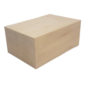 May include: A rectangular wooden block with a light tan color. The block is a solid, geometric shape with visible wood grain. The edges are clean and sharp, suggesting it is freshly cut. This block could be used for crafts or woodworking projects.