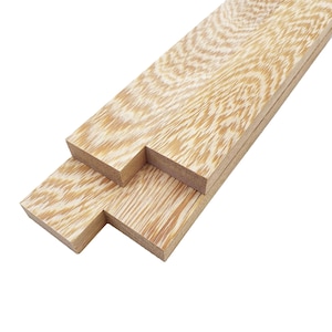May include: Close-up of several light-colored wooden planks with a unique grain pattern. The wood has a natural, warm tone with a mix of light and dark streaks. The planks are cut with a stepped design, suggesting they are for a specific construction purpose.