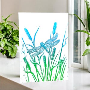Biglietto linoleografico con libellula - suggestiva immagine linoleografica di una libellula tra le canne. Spazio vuoto per il tuo messaggio. Simboleggia il cambiamento. Per gli amanti della fauna selvatica.