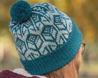 May include: A teal blue knitted beanie with a white and teal patterned design and a fluffy teal pom pom on top.