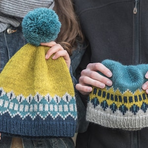 以下が含まれることがあります： 黄色、青、グレーの幾何学模様のニット帽が2つ。1つの帽子には青いポンポンが付いています。
