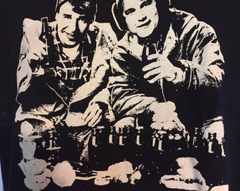 May include: Black and white graphic print of two men wearing winter hats and holding bottles. The text "TAKE OFF, EY" is printed below the image.