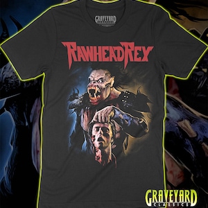 May include: A black short-sleeved t-shirt featuring a graphic print of the monster Rawhead Rex holding a severed human head. The text RAWHEAD REX is printed in red above the creature, and the Graveyard Classics logo is visible at the neck.