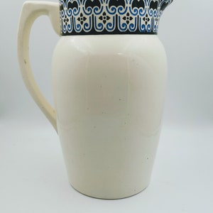 Puede incluir: Jarra de cerámica blanca con un patrón geométrico azul y negro alrededor del borde.