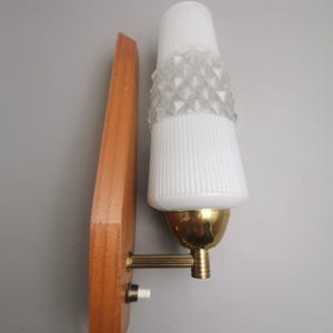 May include: A wall-mounted lamp featuring a vertical wooden backplate with a small white switch. A brass arm extends to hold a conical white glass shade, which displays a textured, diamond-patterned band around its centre and vertical ribbing.