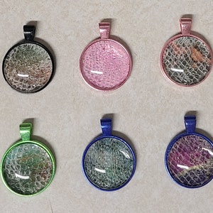 May include: A collection of ten round pendants with various colored frames, including black, pink, green, blue, and bronze. Each pendant features a textured, patterned design under a clear glass dome. The pendants are suitable for jewelry making.