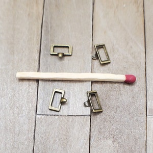 May include: Four small, antique gold-toned metal rectangular drawer pulls with a rounded edge. The pulls have a small loop on the top for attaching to a drawer.