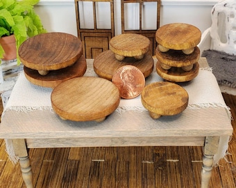 May include: A collection of small, round wooden risers with three small feet. The risers are various sizes and stacked on a small table. The wood has a natural grain and a warm, brown tone. A penny is included for size reference.
