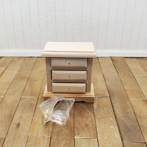 May include: A wooden dresser with three drawers and gold-colored hardware. The dresser is unfinished and ready to be painted or stained. It comes with a small bag of hardware.