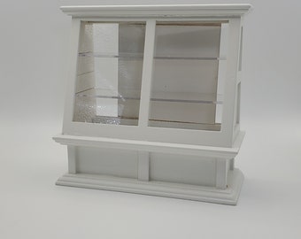 Dollhouse miniature white store display counter cabinet with sliding doors. General store or shop display counter with plexiglass front.