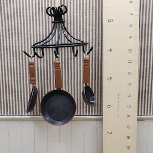 May include: Miniature black metal cookware set with wooden handles, including a frying pan and two utensils, hanging from a decorative black metal rack. The frying pan measures approximately 2 inches in diameter.