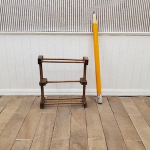 May include: A miniature wooden rack with two tiers and a large yellow pencil with a silver eraser. The pencil is positioned vertically next to the rack. The rack is made of dark brown wood and has a simple design.