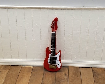 May include: A red electric guitar with white accents and a black pickguard. The guitar is on a wooden floor.