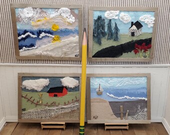 May include: Four framed fabric art pieces with a yellow pencil in front. The art pieces are all different scenes, including a seascape, a forest, a farm, and a beach. Each piece is framed in a simple wooden frame.