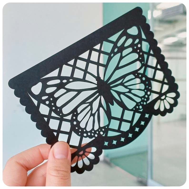 K&ouml;nnte beinhalten: Schwarzer Papierschnitt eines Schmetterlings mit filigranen Details. Der Schmetterling ist von einem Gittermuster umgeben und hat einen gewellten Rand.