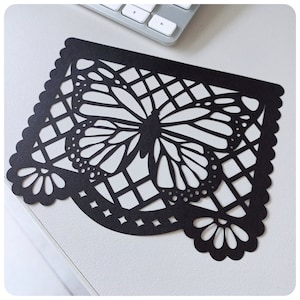 K&ouml;nnte beinhalten: Schwarzer Papierschnitt eines Schmetterlings mit geometrischem Muster. Der Schmetterling ist mittig im Ausschnitt platziert und hat ein detailliertes Design.