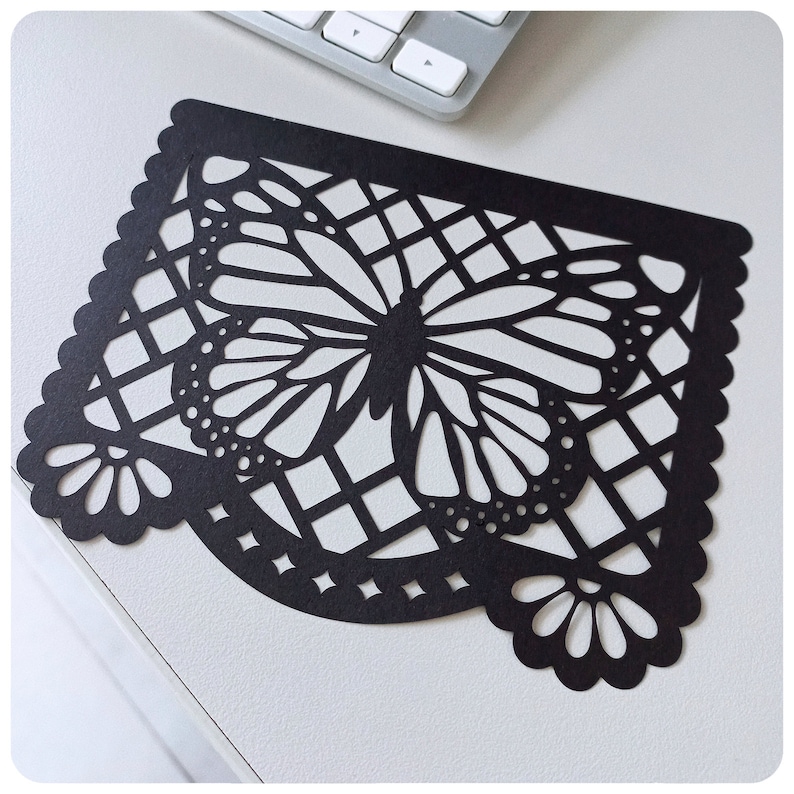 K&ouml;nnte beinhalten: Schwarzer Papierschnitt eines Schmetterlings mit geometrischem Muster. Der Schmetterling ist mittig im Ausschnitt platziert und hat ein detailliertes Design.