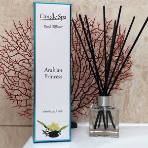 May include: A white box with the text "Candle Spa Reed Diffuser Arabian Princess 100ml (3.38 fl oz) e" and a clear glass bottle with black reeds and the text "Candle Spa" on the label.