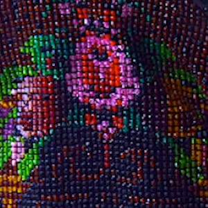 May include: Close-up of a beaded fabric with a floral pattern. The fabric is made of small, colorful beads in shades of pink, red, green, and brown. The beads are arranged in a repeating pattern of flowers and leaves.
