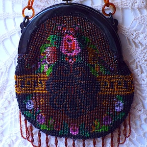 May include: A vintage beaded purse with a floral design and a black frame. The purse has a long chain strap and a fringe detail.