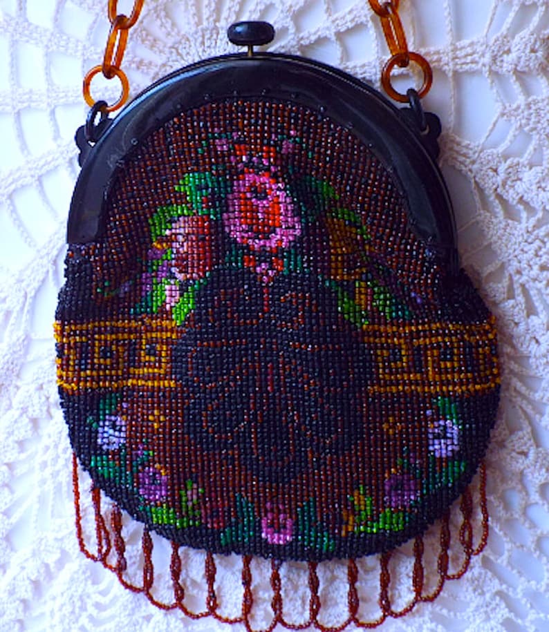 May include: A vintage beaded purse with a floral design and a black frame. The purse has a long chain strap and a fringe detail.