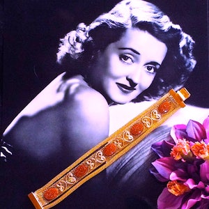 May include: A gold bracelet with a chain link design and orange stones. The bracelet is on a black and white background.