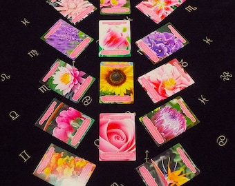 May include: A set of 12 tarot cards featuring different flowers, each card has a zodiac symbol in the corner. The cards are laid out in a circle on a black background.