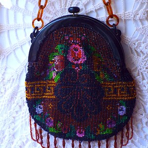 May include: A vintage beaded purse with a floral design and a brown plastic chain strap. The purse is round and has a black plastic frame.