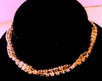 May include: A gold chain necklace with clear rhinestones. The necklace is on a black velvet display stand.