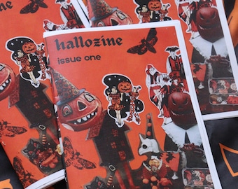 Op de afbeelding: Twee exemplaren van een zine getiteld hallozine issue one, met een feloranje omslag en zwarte illustraties van pompoenen, motten, een nar en een huis. Het ontwerp bevat diverse vintage-stijl afbeeldingen en tekst in een vetgedrukt zwart lettertype.