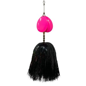 May include: A fishing lure with two bright pink, teardrop-shaped blades above a black, fringed skirt. The lure is suspended by a thin metal wire and small beads.