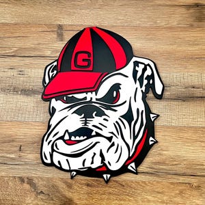 May include: A decorative bulldog head with a red and black baseball cap featuring a large letter "G". The bulldog is white with black and red accents, including a spiked collar. The image is a cut-out design.
