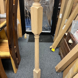 May include: A tall, unfinished wooden newel post with a ball finial. The post has a square base, a long octagonal body, and a turned section. The wood grain is visible. The post is designed for a staircase.