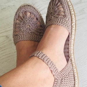 May include: A pair of crocheted sandals with a delicate floral design. The sandals are a light brown color and have a flat sole.