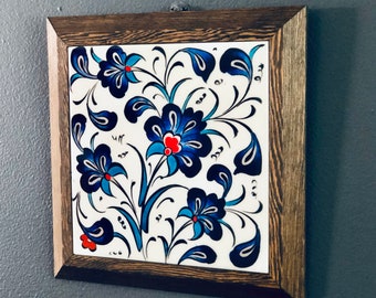 May include: A framed ceramic tile with a blue and white floral design. The tile features intricate floral patterns with blue and white accents, and a red center.