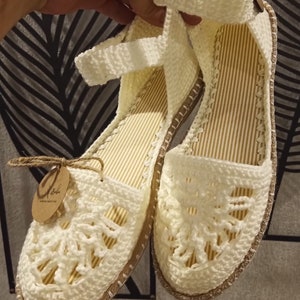 May include: White crocheted sandals with a delicate floral design. The sandals have a brown jute sole and a white strap that goes around the ankle. The sandals are handmade and have a tag that says "Handmade with love".