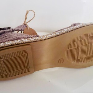 May include: The bottom of a crocheted sandal with a brown sole and a white trim. The sole has a textured pattern.