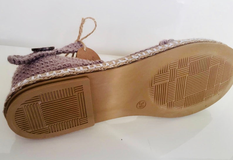 May include: The bottom of a crocheted sandal with a brown sole and a white trim. The sole has a textured pattern.