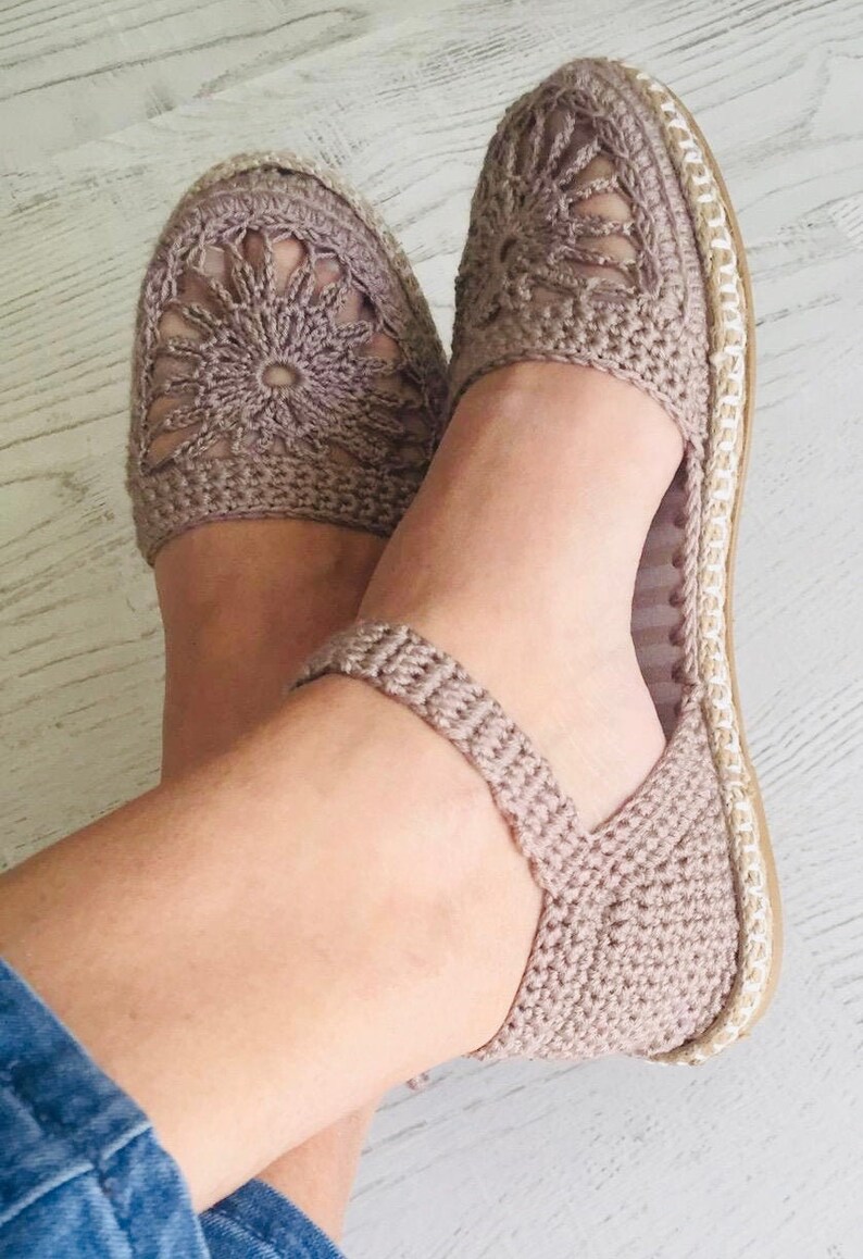 May include: A pair of crocheted sandals with a delicate floral design. The sandals are a light brown color and have a flat sole.