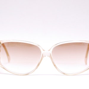 May include: Clear plastic sunglasses with a brown gradient lens. The sunglasses have a square shape with rounded edges.