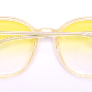 May include: Yellow plastic framed sunglasses with a gradient yellow lens. The sunglasses have a white and yellow striped pattern on the arms.