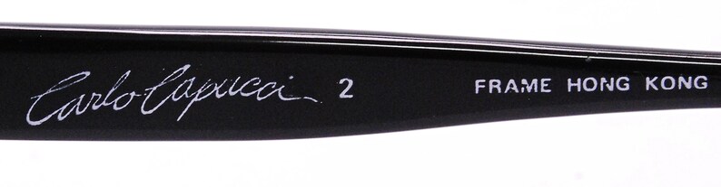 May include: Close-up of the black frame of a pair of eyeglasses with the text "Carlo Zucchi 2 FRAME HONG KONG" printed in white.