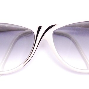 May include: White cat-eye sunglasses with black trim and gradient grey lenses.